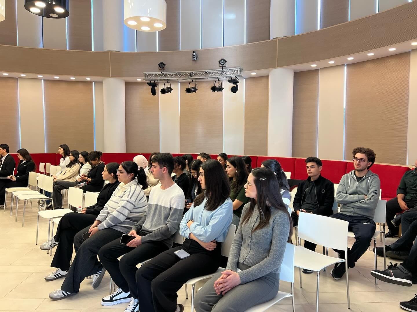 Students seated in rows in a bright hall, following the debate.