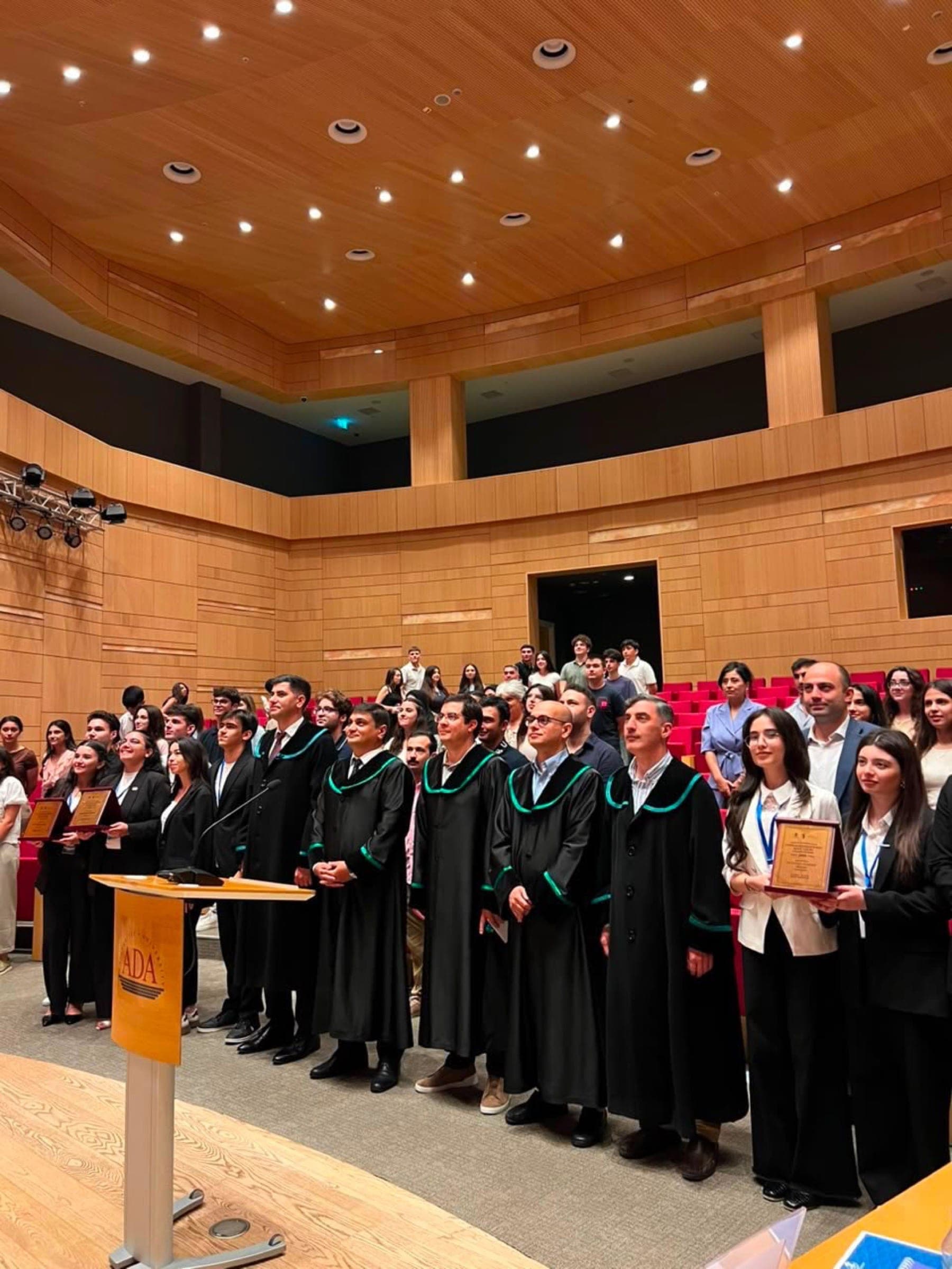 Participants in academic robes standing together on the auditorium stage at the close of the competition.