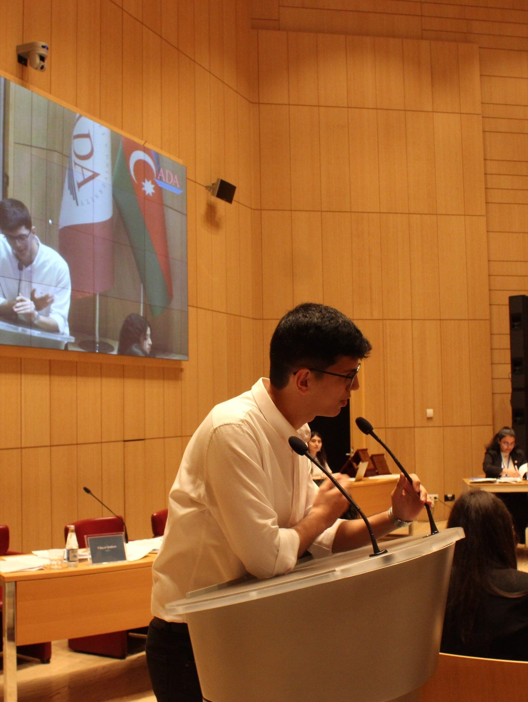 A participant making oral submissions at a microphone; the screen behind shows the bench and the flag of Azerbaijan.