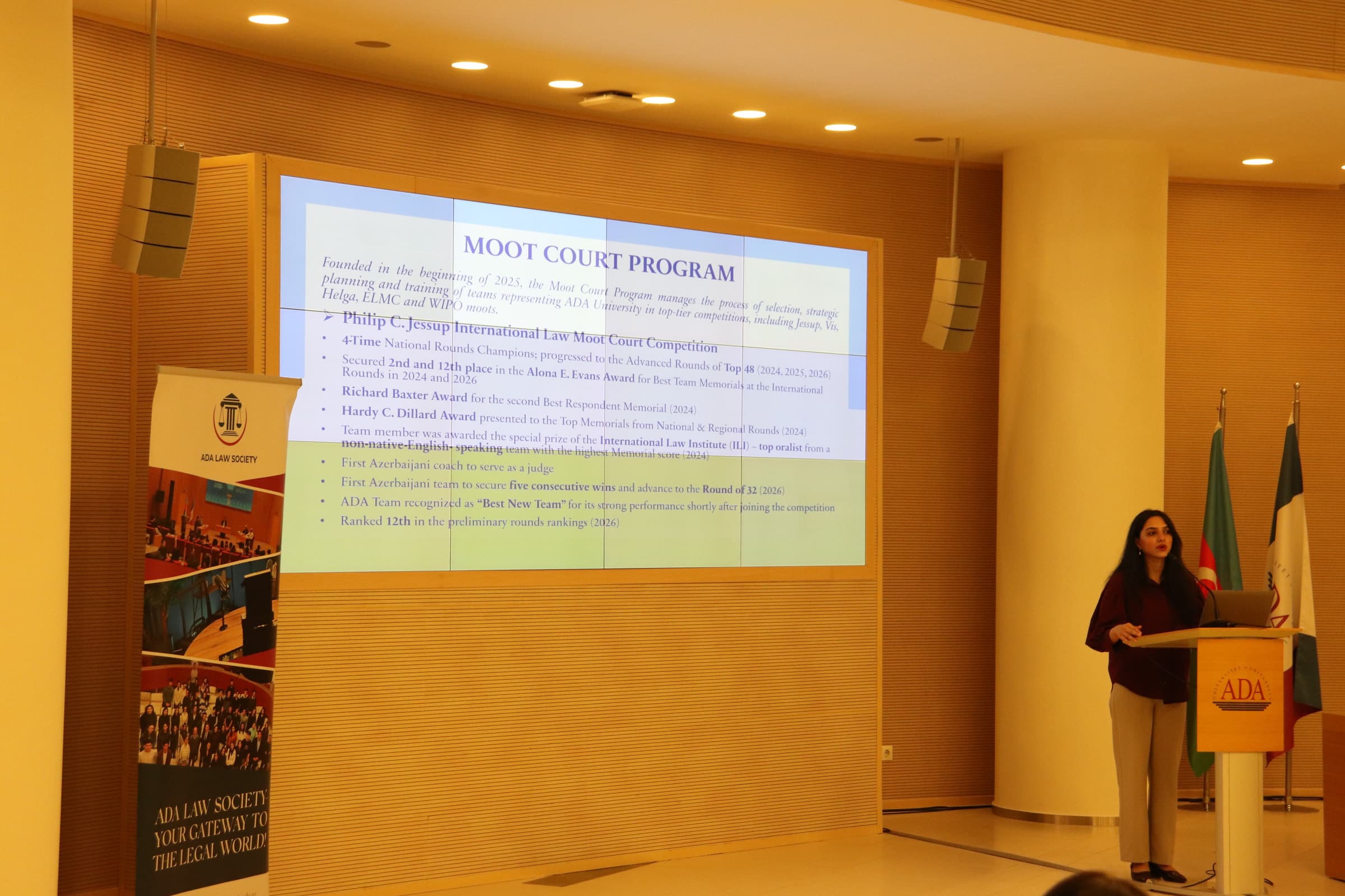 A slide on the moot court programme projected above the stage, with the ADA Law Society banner at its side.
