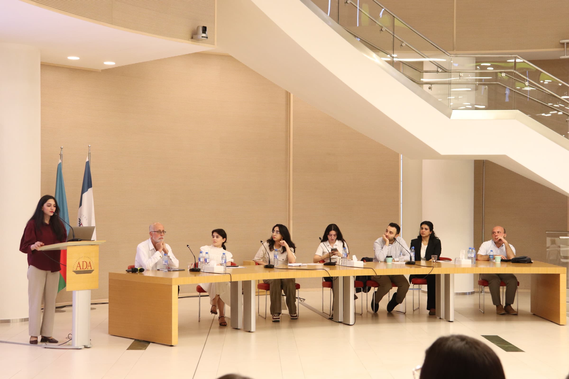 A speaker at the lectern, with the panel seated along a long table.