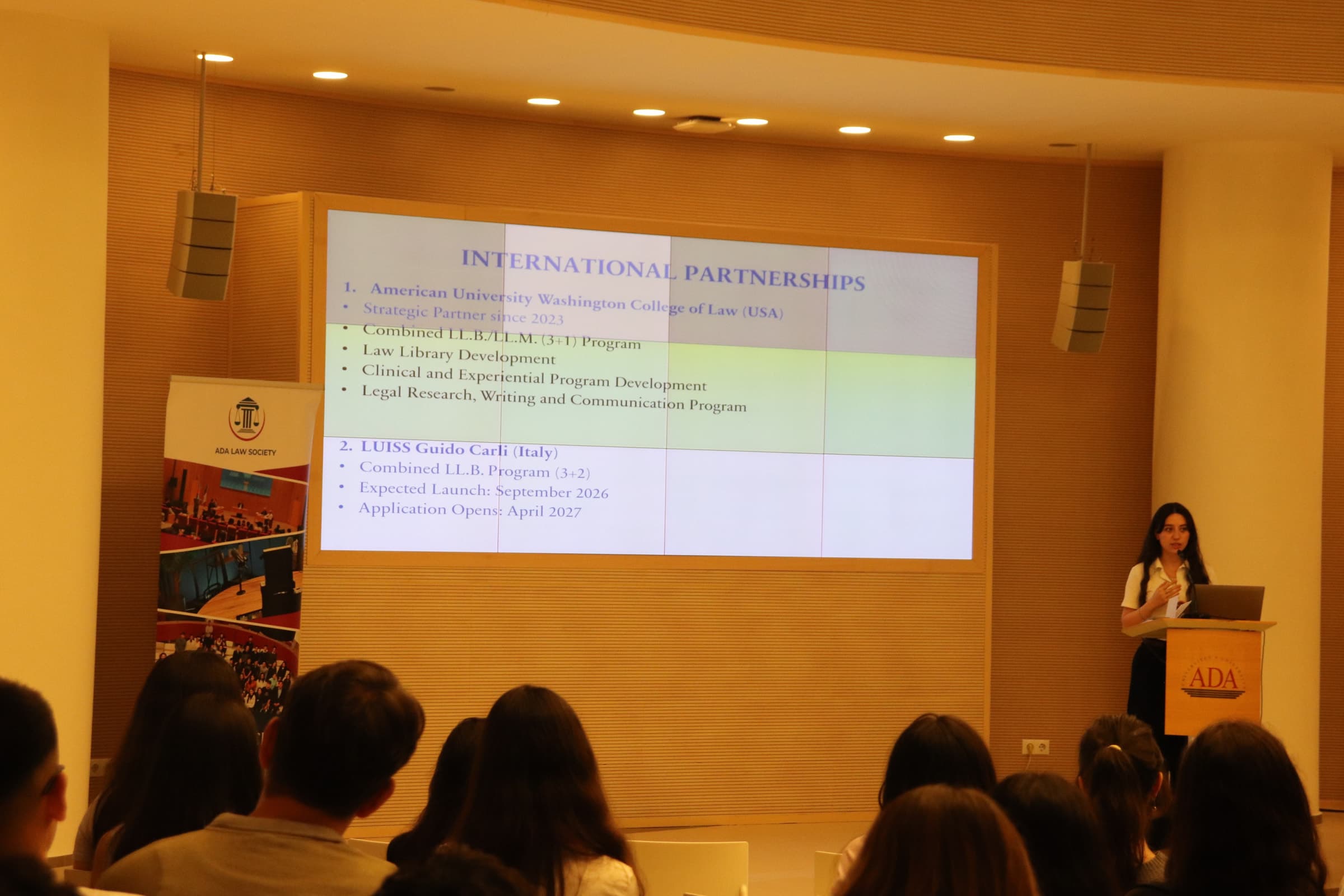 A slide on international partnerships projected above the stage, with the ADA Law Society banner at its side.