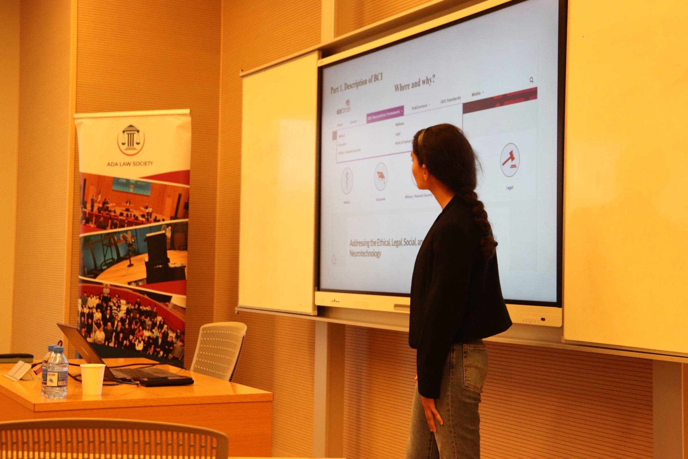 A speaker standing at the screen mid-presentation, the Society banner visible at the edge of the room.