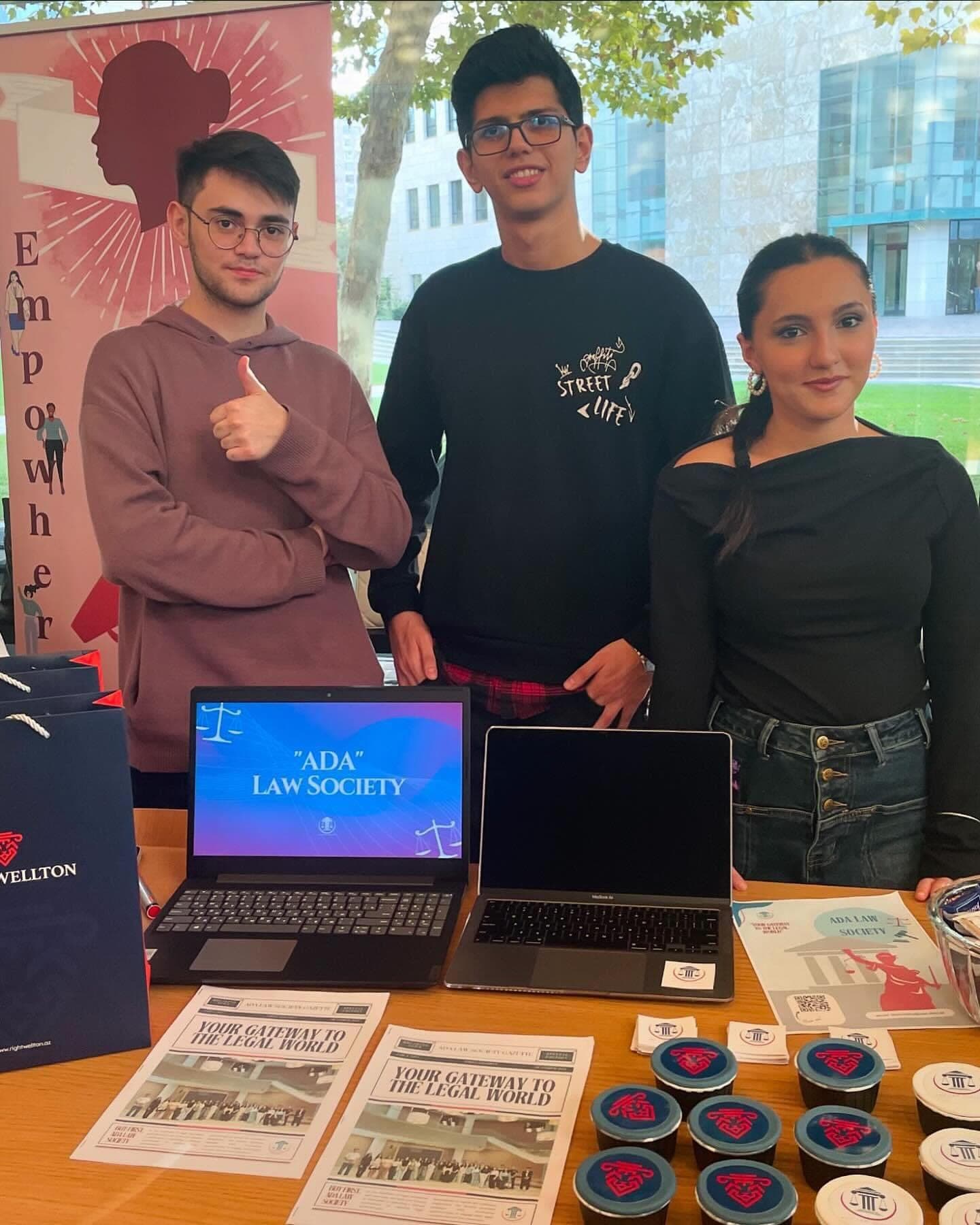 The Society’s stand: a laptop showing “ADA Law Society” on screen beside a second laptop and printed materials, with students gathered around.