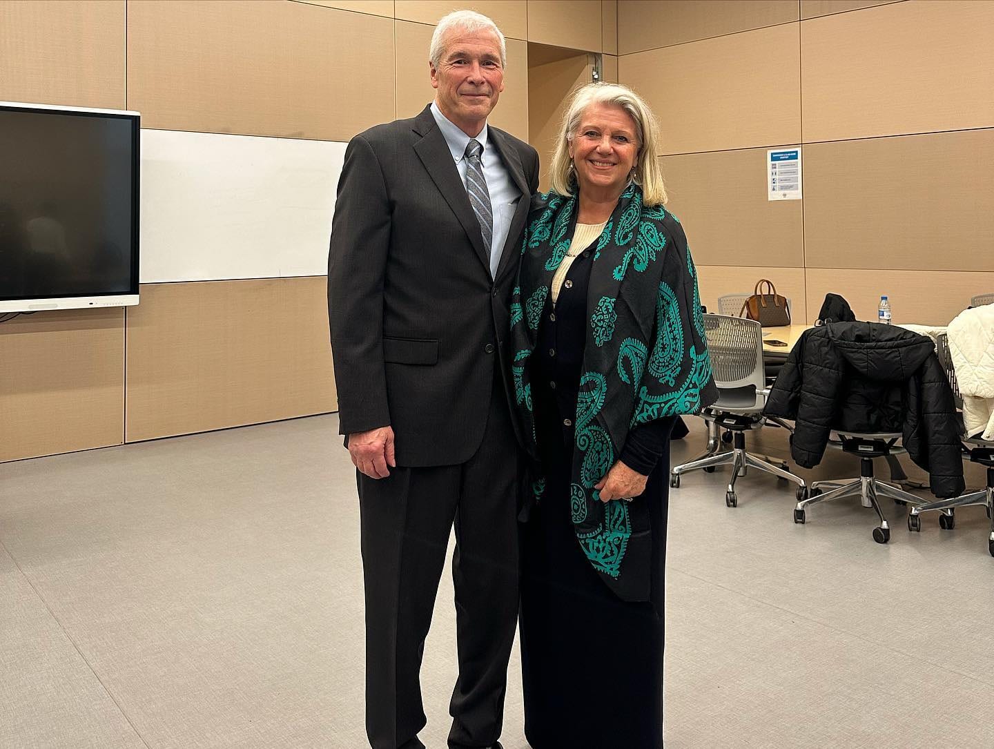 A man in a dark suit and a woman in a black shawl patterned in green stand side by side in an ADA University classroom.
