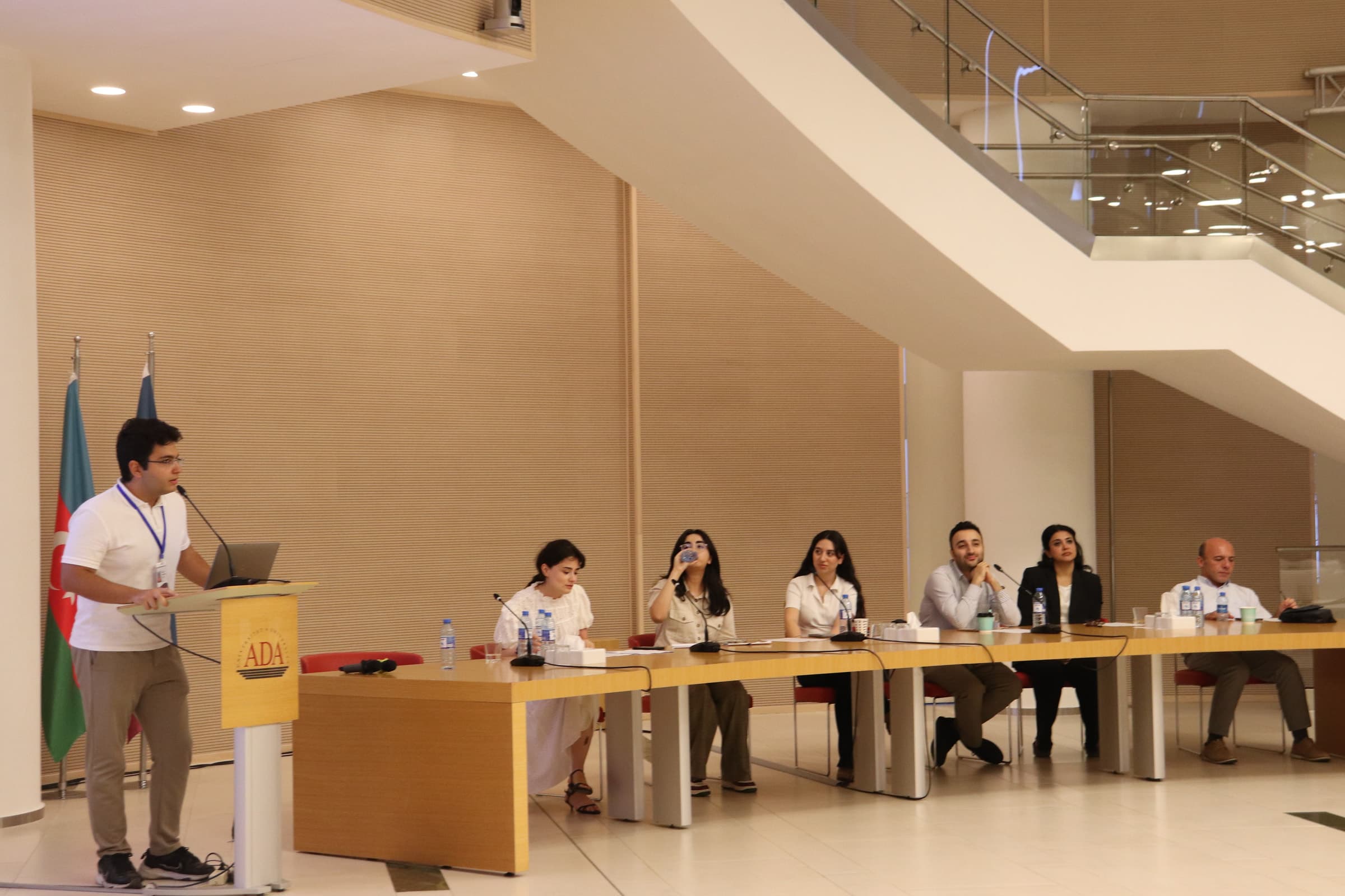 A presenter at the lectern and the School of Law panel seated along a long table in the hall.